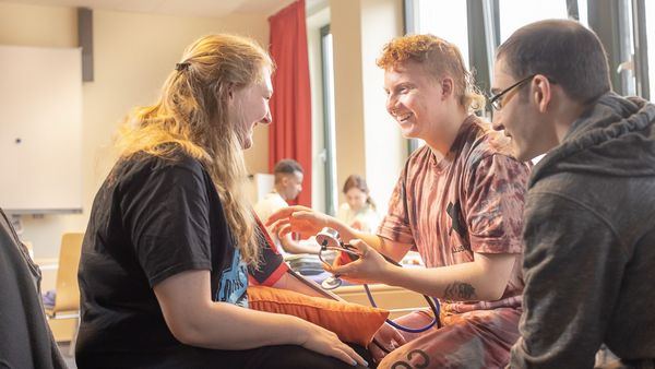 Eine Schülerin und zwei Schüler üben Blutdruckmessen.